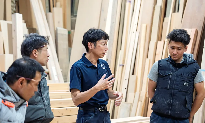 材木に囲まれた作業場で打ち合わせをする岩木建築の大工たち