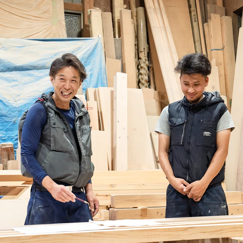 作業場で材を前に話す2人の大工