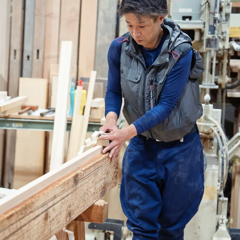 作業場で長い材を手に取る大工